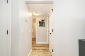 A narrow hallway with wooden flooring, white walls, and a ceiling light fixture. - Fremont Stylish Stay | Near K-State | Free Parking (Manhattan)