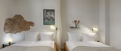 Une chambre d’hôtel avec deux lits, un mur en briques apparentes, une affiche accrochée au mur et une petite étagère avec des fleurs.