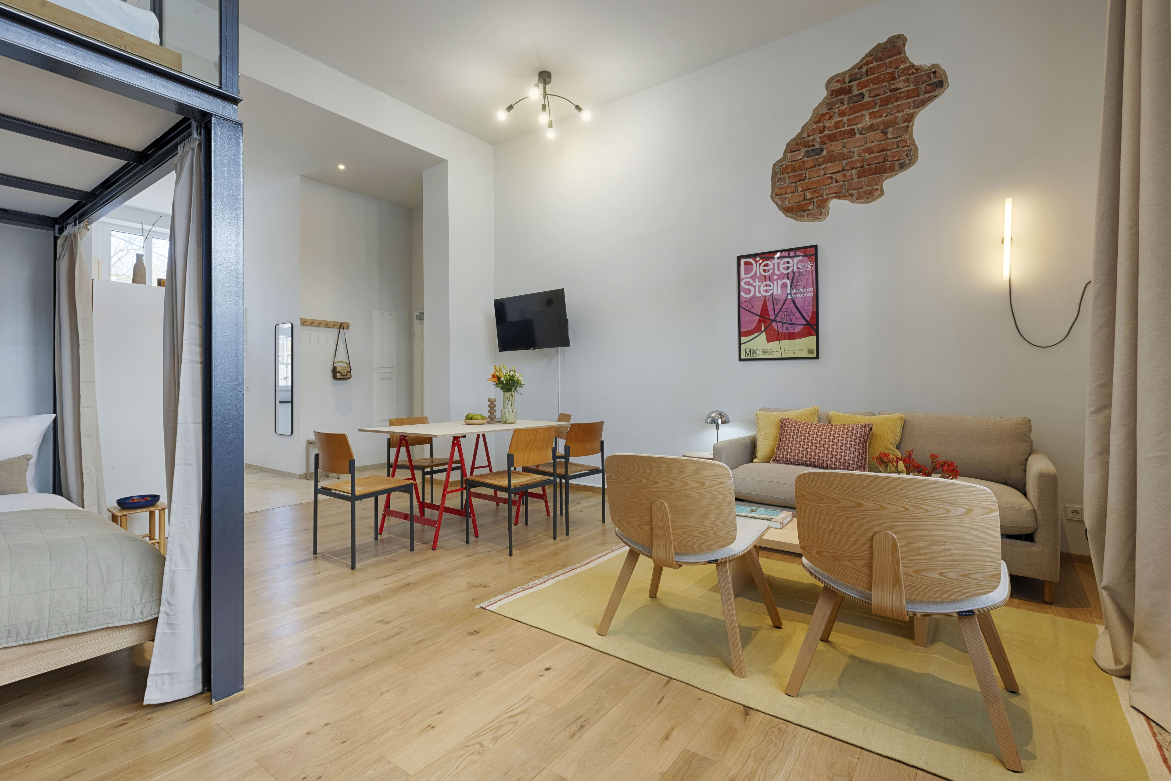 A modern living room with a dining area, a flat-screen TV mounted on the wall, and a brick accent wall.