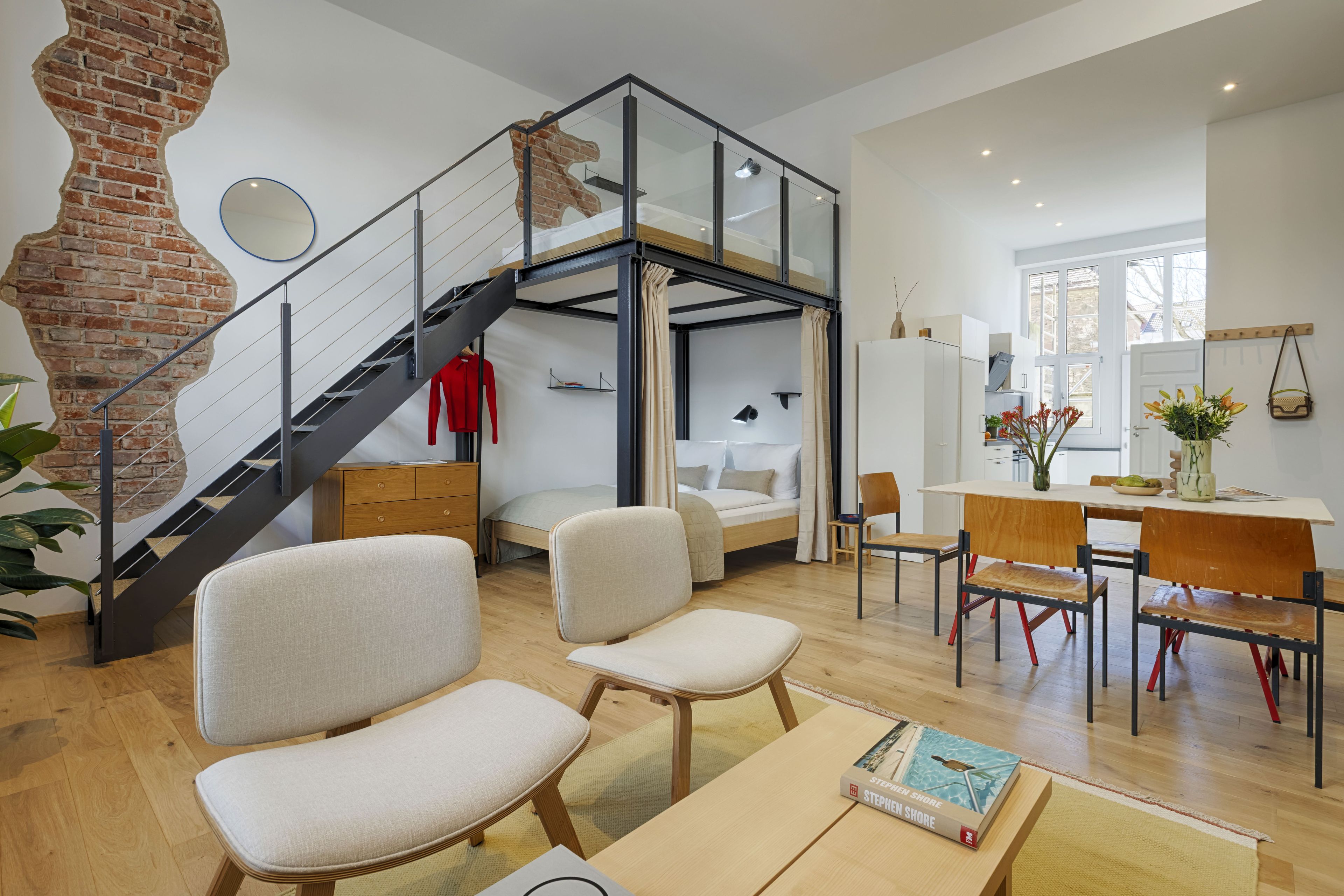 A modern interior with a loft bedroom, a dining area, and a staircase.