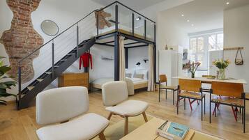 A modern interior with a loft bedroom, a dining area, and a staircase.