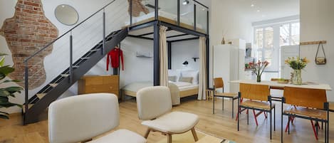 A modern interior with a loft bedroom, a dining area, and a staircase.
