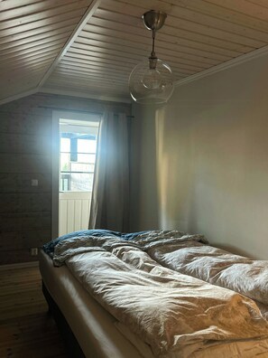 Un dormitorio con techo inclinado, una cama con edredón estampado, una ventana con cortinas y una lámpara colgante.
