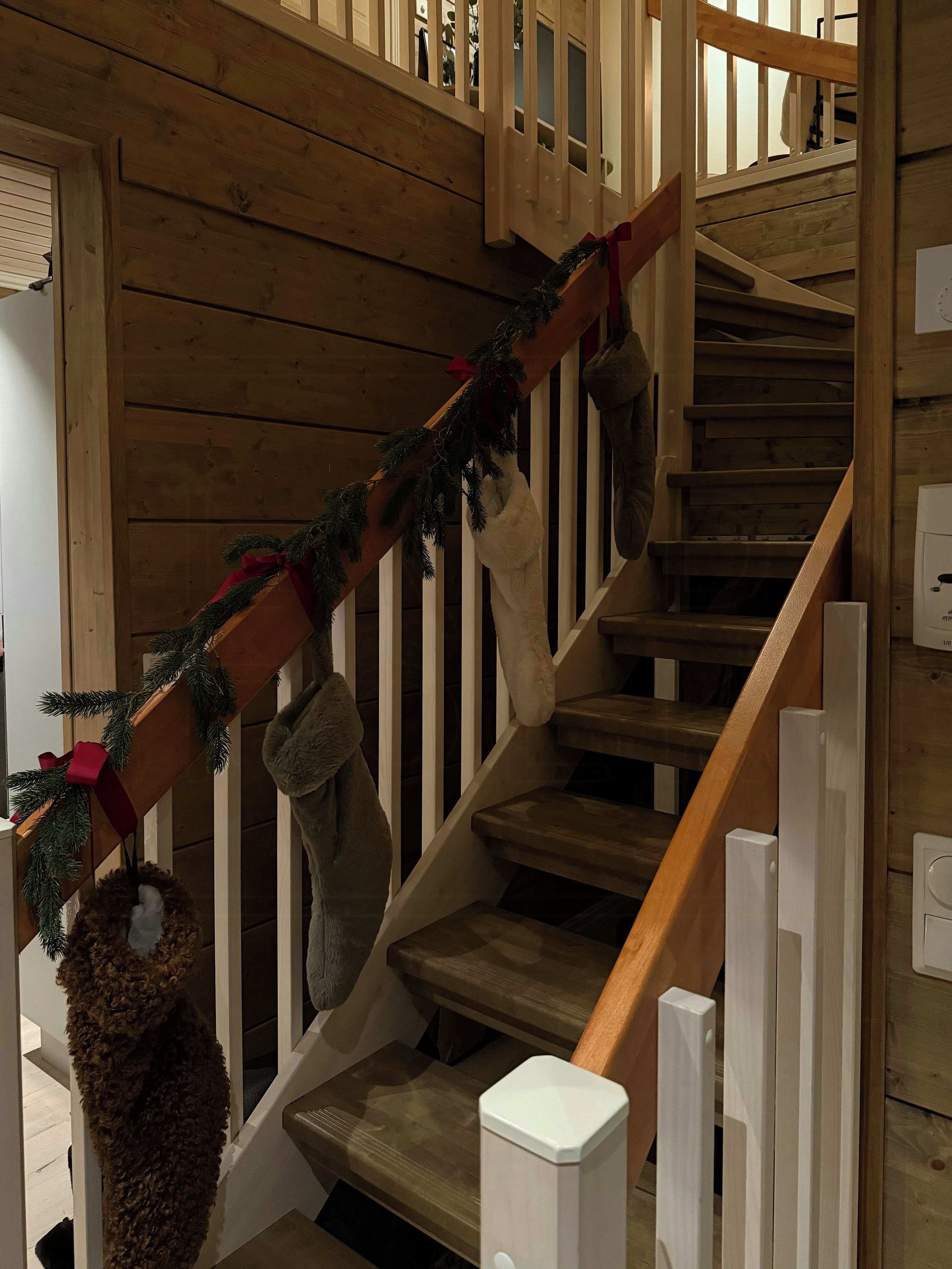 Una escalera de madera con barandilla, una guirnalda navideña y un par de botas colgadas del pasamanos.