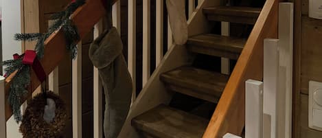 A wooden staircase with a handrail, a Christmas garland, and a pair of boots hanging on the railing.