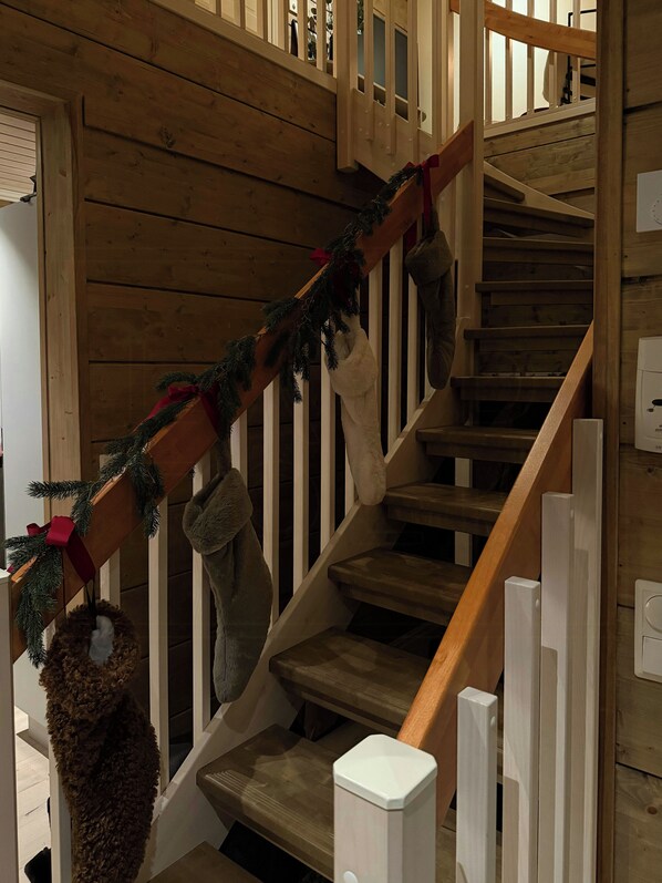 Una escalera de madera con barandilla, una guirnalda navideña y un par de botas colgadas del pasamanos.