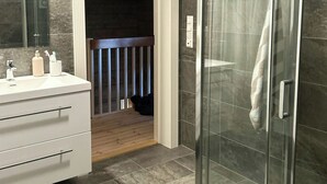 A modern bathroom with a glass shower enclosure, a white vanity with drawers, and a wooden floor.