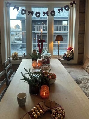 Una mesa de comedor dispuesta con velas, un árbol de Navidad y una zona de estar acogedora con una lámpara.