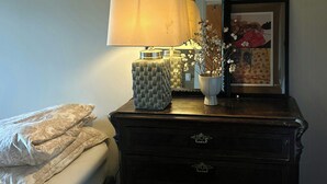 A bed with a blanket, a dresser with drawers, a lamp, a vase with flowers, and a framed picture on the wall.