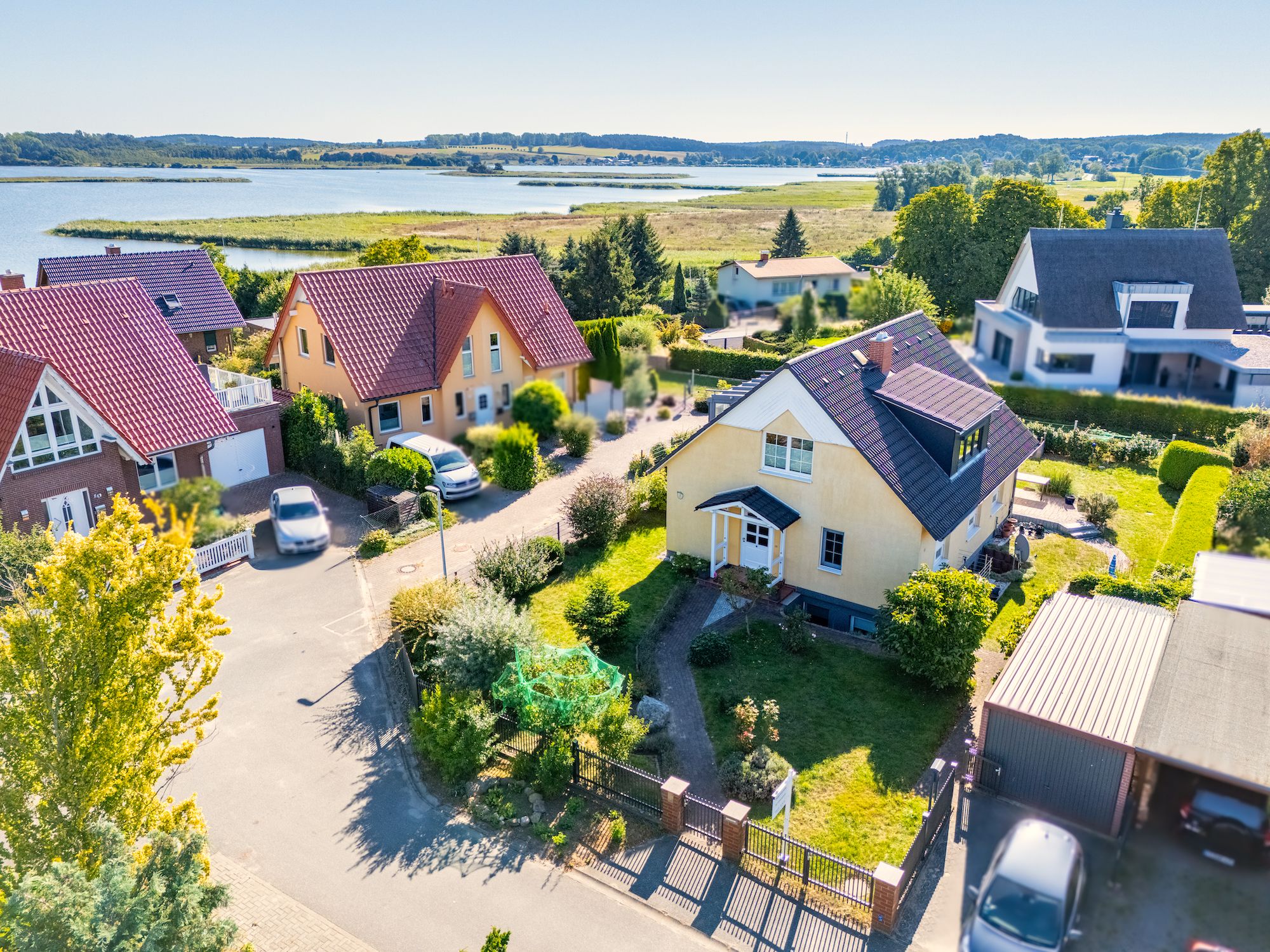 A residential area with houses, a road, and a lake in the background.