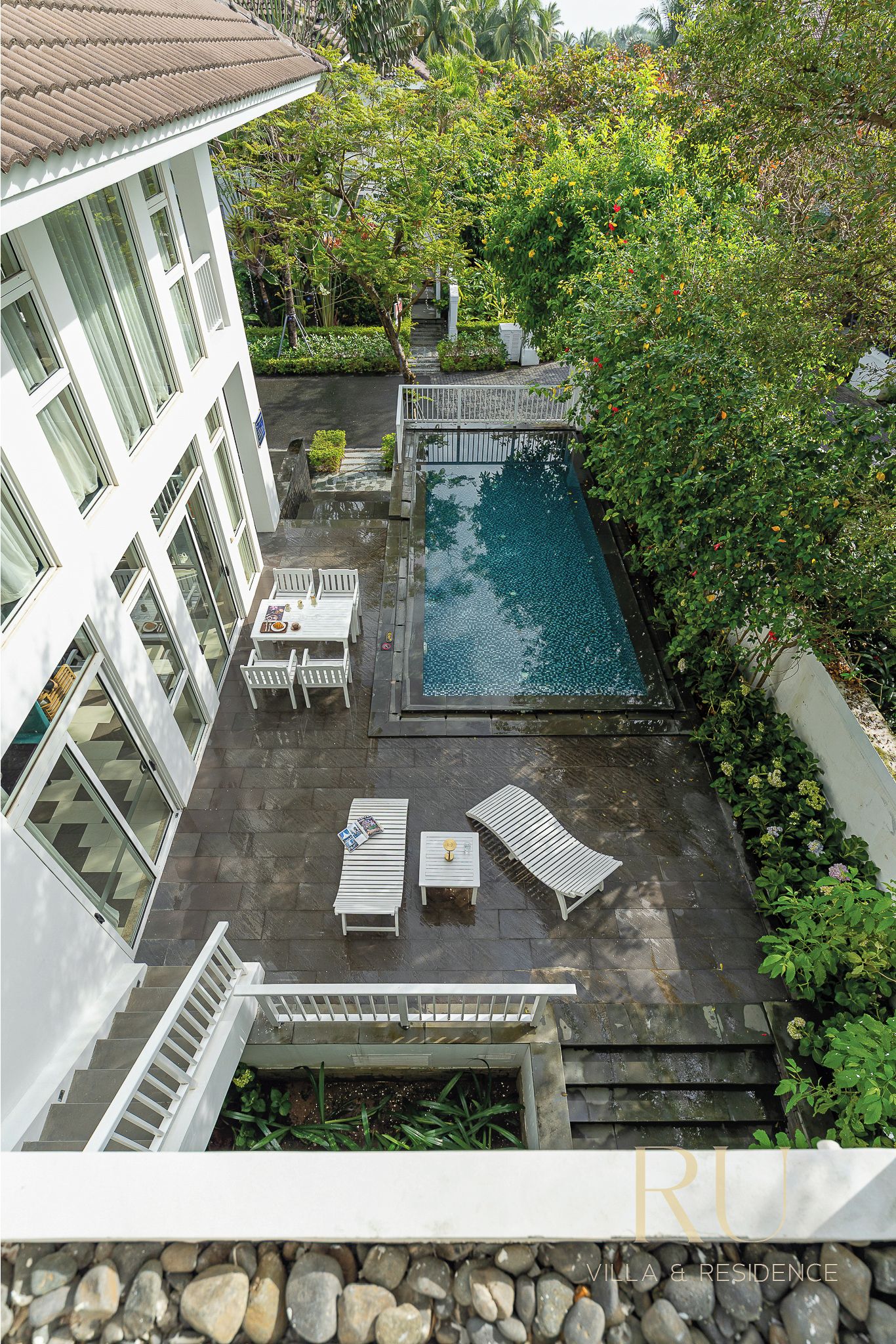 A rooftop pool area with lounge chairs and a table, surrounded by greenery.