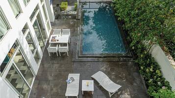A rooftop pool area with lounge chairs and a table, surrounded by greenery.