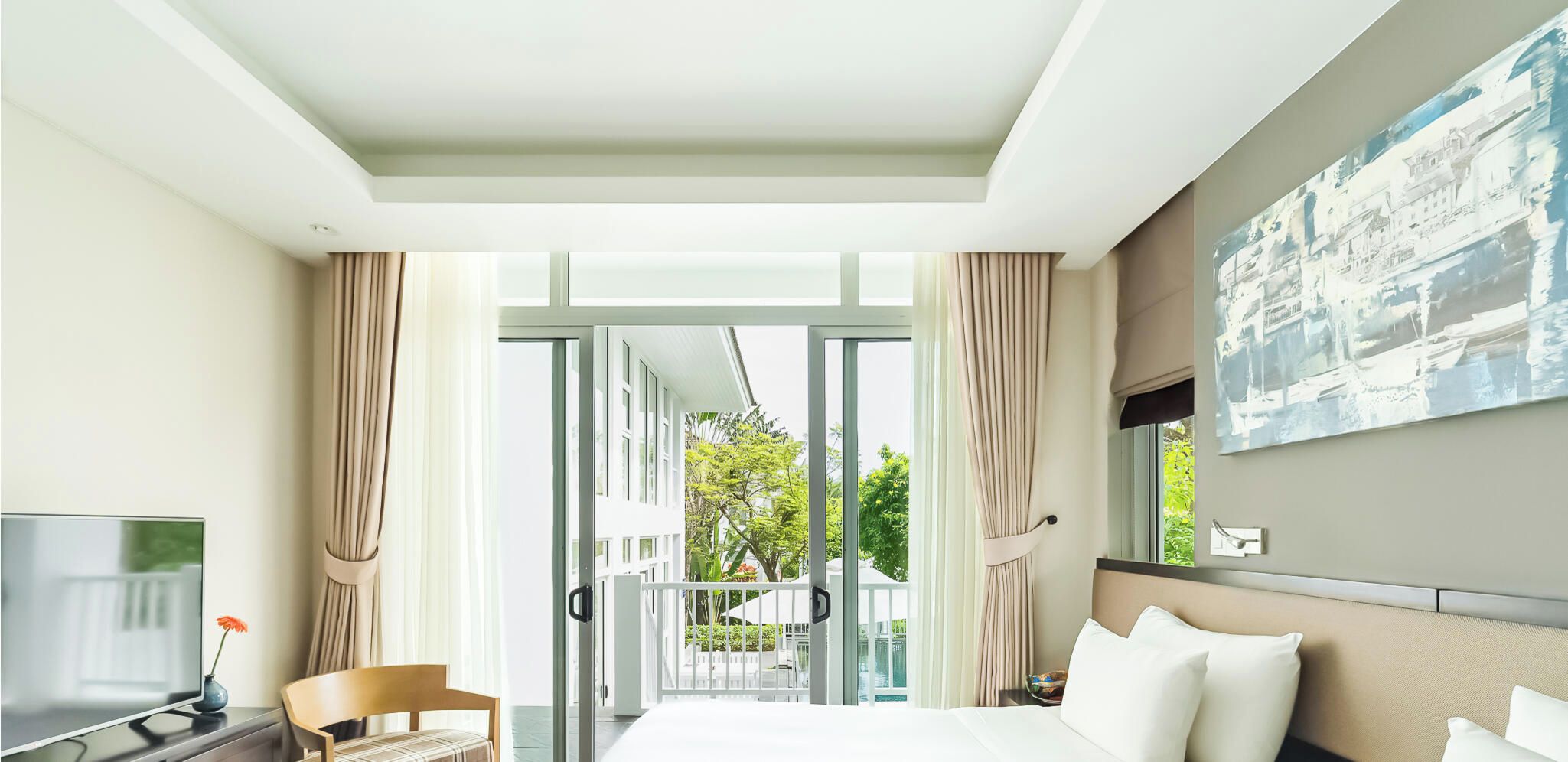 A hotel room with a bed, a TV, a desk, and a balcony with curtains.