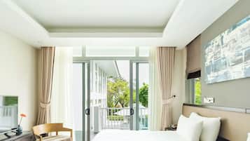 A hotel room with a bed, a TV, a desk, and a balcony with curtains.