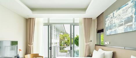 A hotel room with a bed, a TV, a desk, and a balcony with curtains.