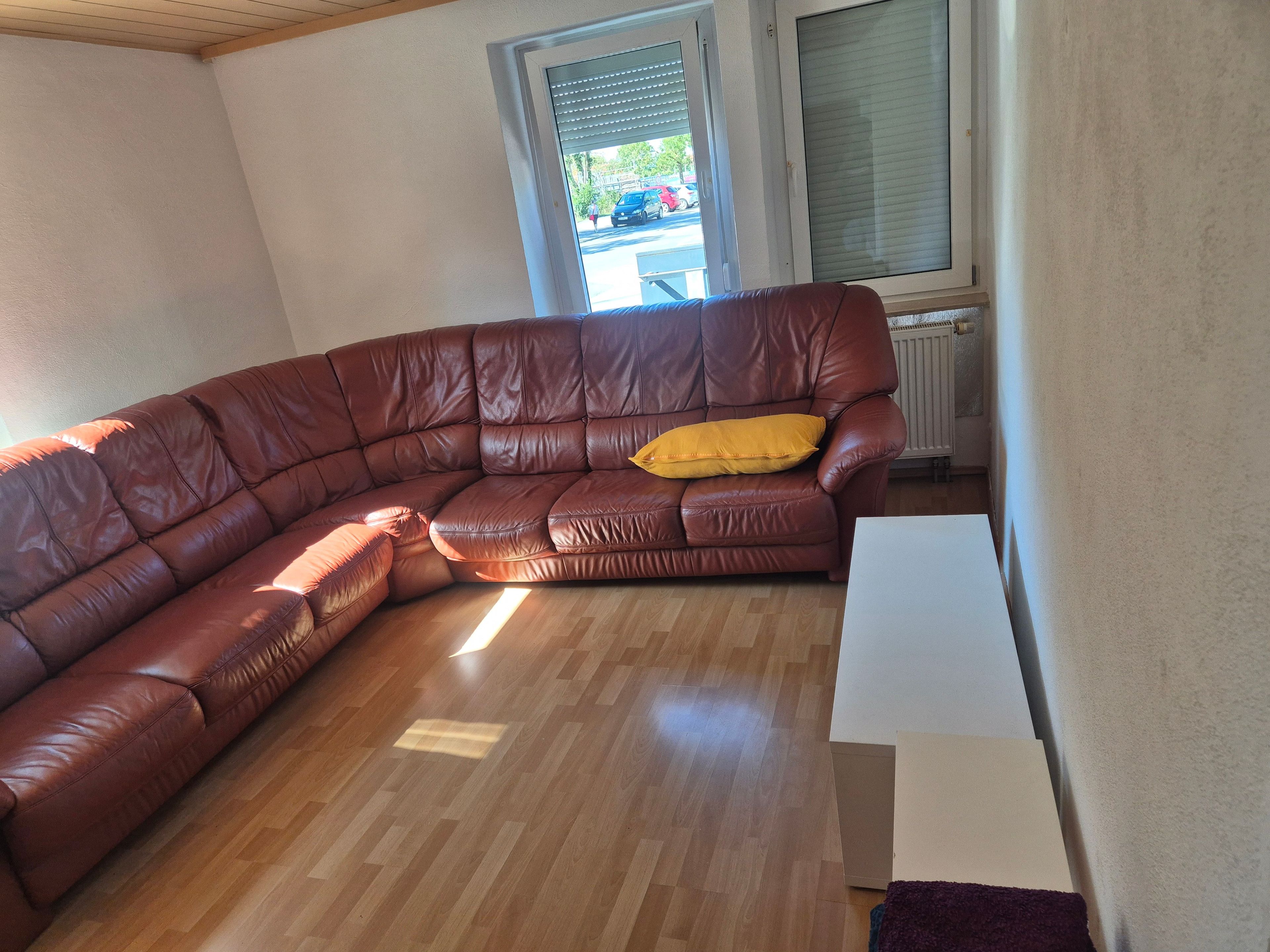 A brown leather sectional sofa with a yellow pillow, a white table, and a window with blinds.