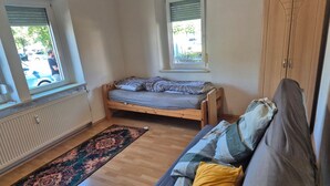 A room with a bed, a sofa, a window, a radiator, and a wooden wardrobe. - Reichsstadtappart. Rothenburg o.T. – 4 Bedrooms, Central Location (Rothenburg ob der Tauber)