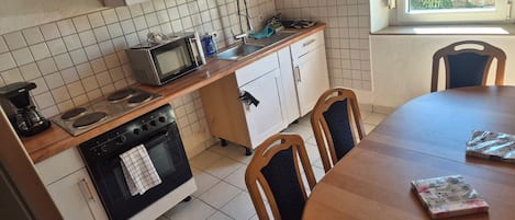A kitchen with a stove, microwave, and sink. There is a dining table with chairs.