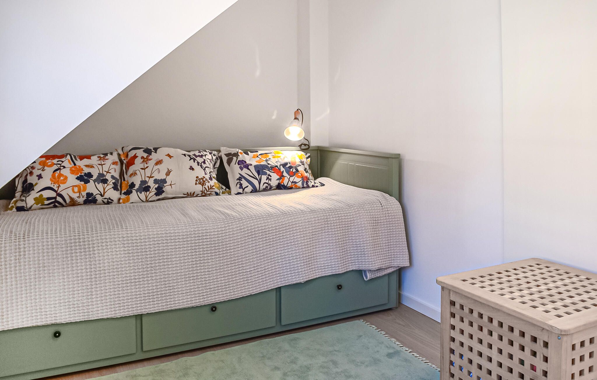 Une chambre à coucher avec un lit, des oreillers, une lampe de chevet, une tête de lit verte et un petit tabouret en bois.