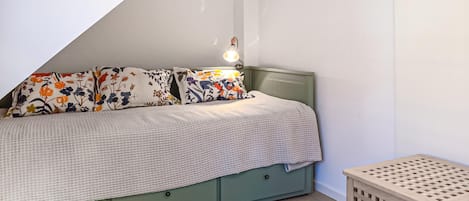 A bedroom with a bed, pillows, a bedside lamp, a green headboard, and a small wooden stool.