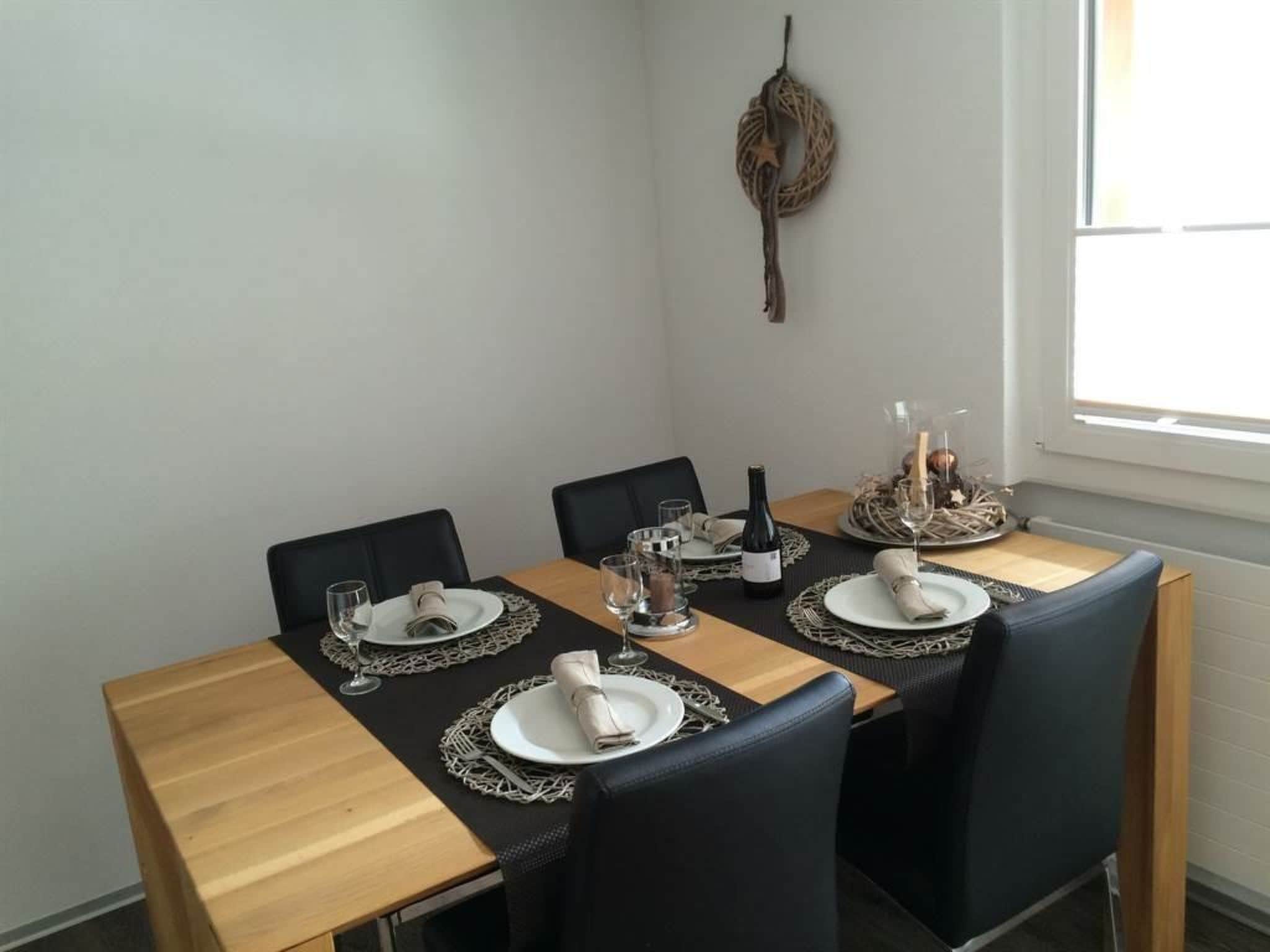 A dining table set for four with black chairs, a woven wall hanging, and a window with natural light.