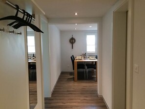 A hallway leading to a dining area with a table and chairs, a coat rack, and a wall-mounted light fixture. - Bergfreude Kuonen Appartement/Fewo 4-Bettwohnung by Interhome (Saas-Grund)