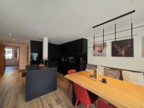 A modern kitchen with a central island, black cabinetry, and a dining area with a wooden table and red chairs. - Du Glacier A3 Appartement/Fewo Appartement/Fewo by Interhome (Saas-Fee)