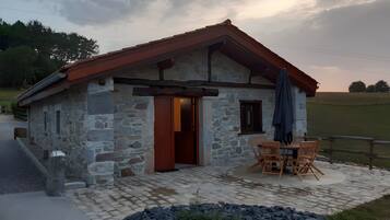 Un edificio in pietra con tetto rosso, una porta di legno e un tavolo con sedie all'esterno.