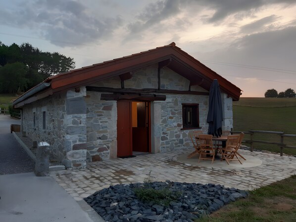 A stone building with a red roof, a wooden door, and a table with chairs outside. - Holiday Home "Maison Gau Argi2" with Wi-Fi (Armendarits)