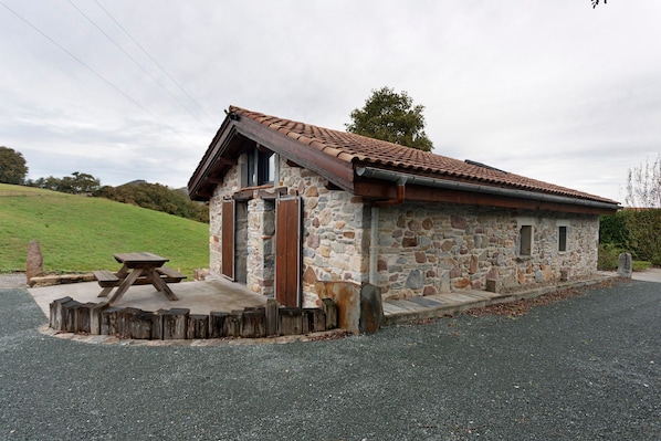 A stone building with a tiled roof, a wooden bench, and a gravel driveway.