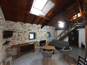 A cozy room with a stone wall, a wooden ceiling, a sofa, a table, and two chairs. - Holiday Home "Maison Gau Argi2" with Wi-Fi (Armendarits)