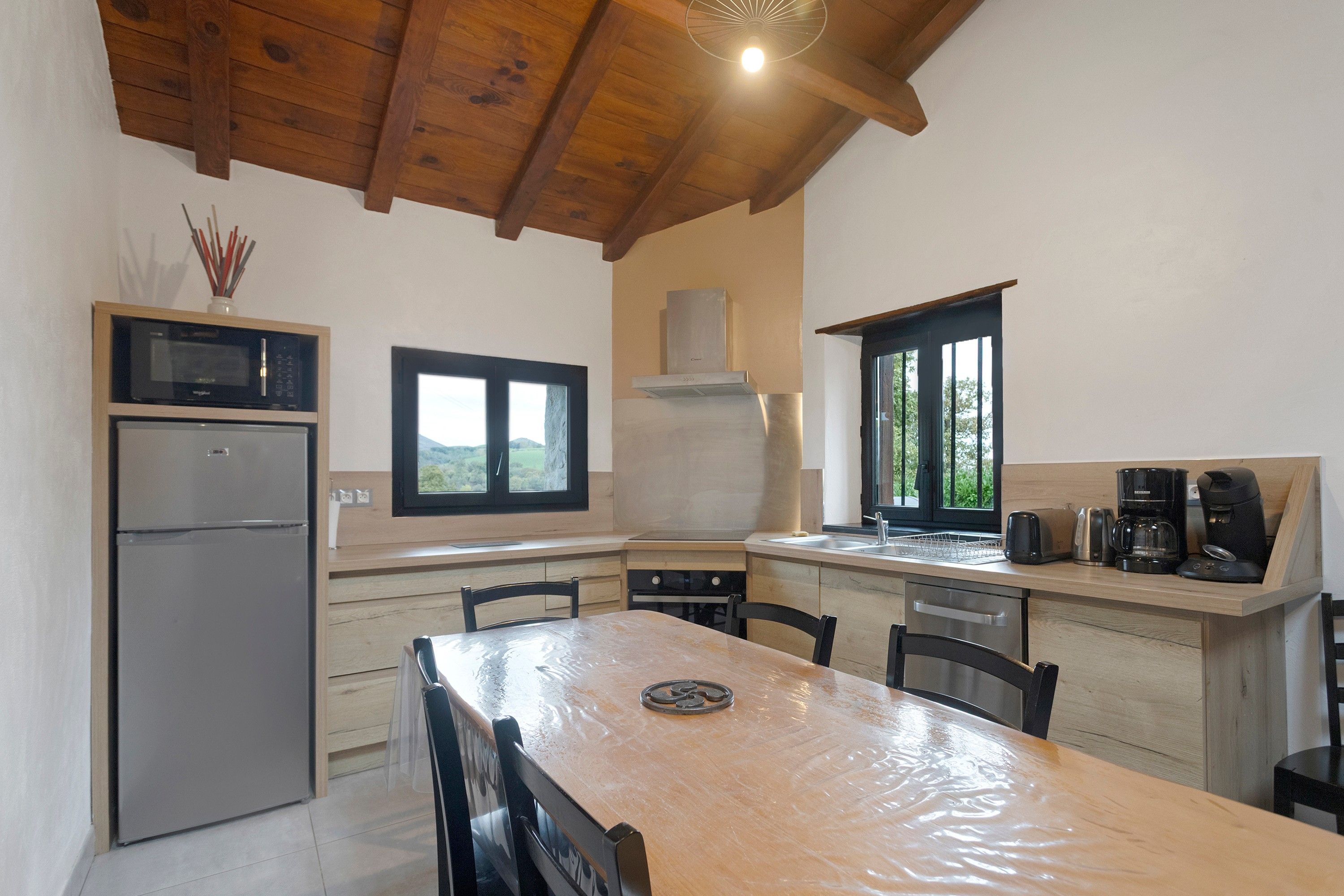 A modern kitchen with a wooden ceiling, a refrigerator, a microwave, a stove, and a coffee maker.