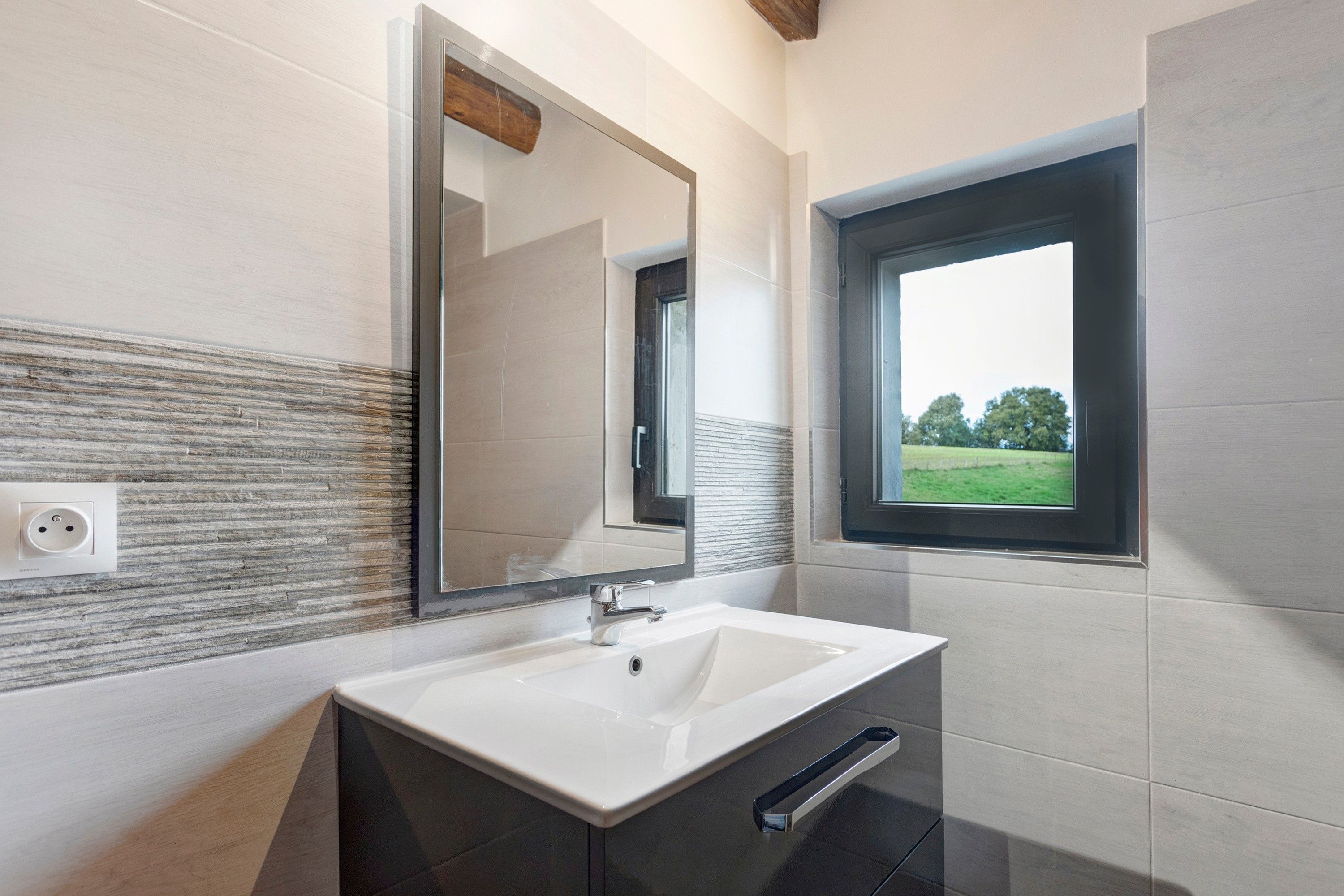 A bathroom with a large mirror, a window, and a sink.