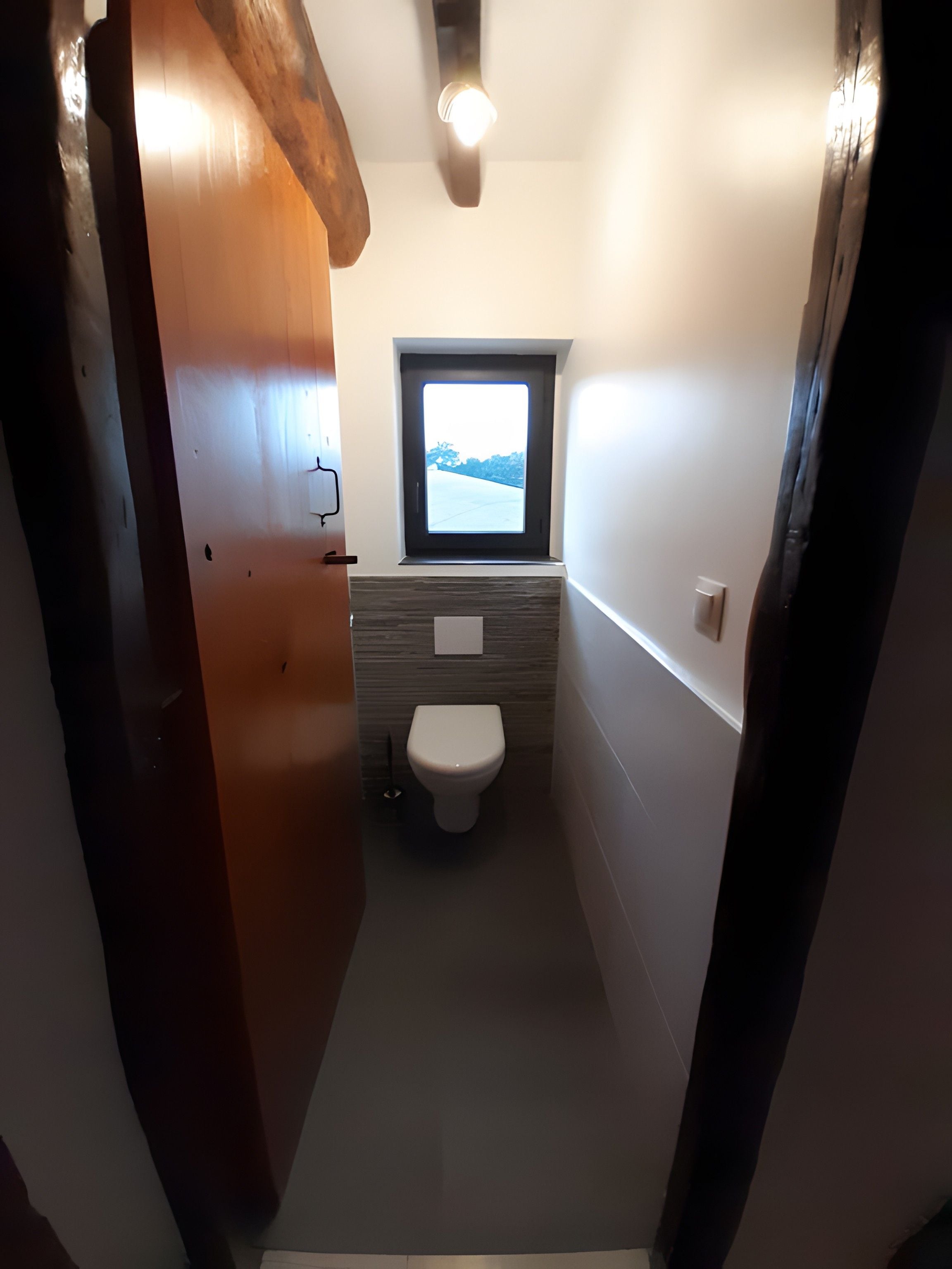 A narrow hallway leading to a bathroom with a window, a toilet, and a small sink.