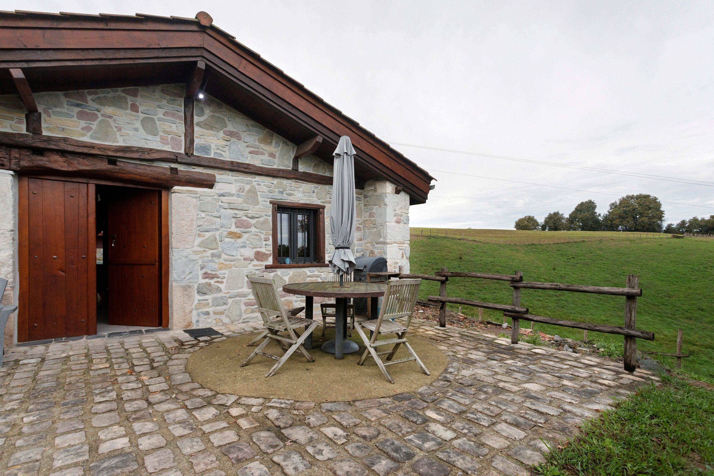A stone building with a wooden door, a window, and a barbecue grill outside.
