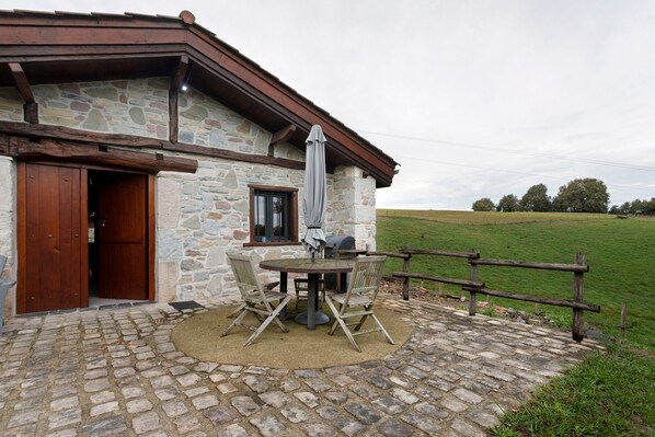 Un edificio de piedra con puerta de madera, una ventana y una parrilla al aire libre.