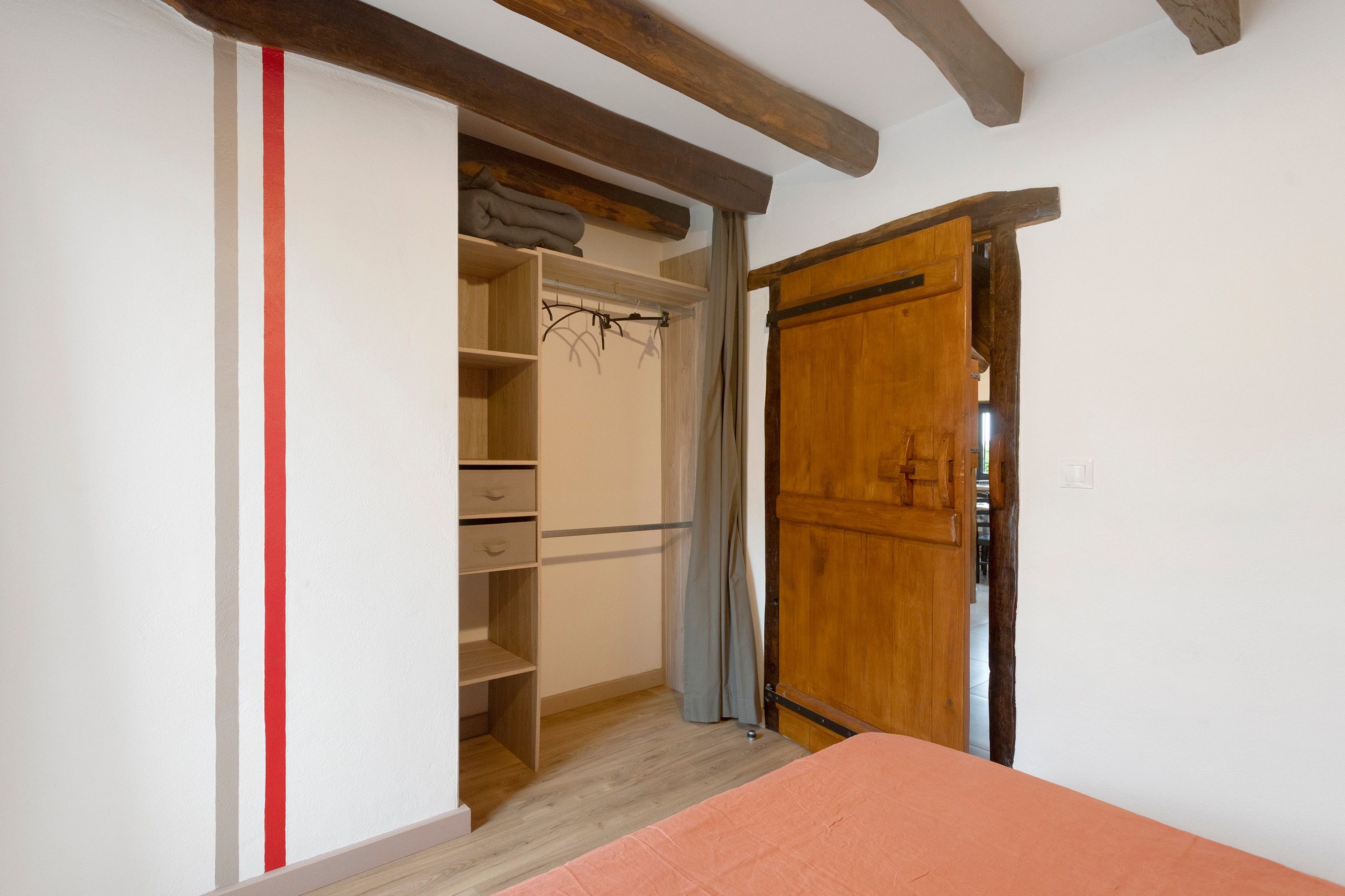 A bedroom with a wooden wardrobe, a bed with a pink bedspread, and a closet with hanging space.