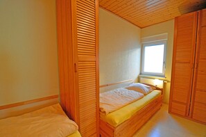 Ein Schlafzimmer mit einem Einzelbett, einem Holzschrank und einem Fenster, das für natürliches Licht sorgt.