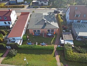 Ein Wohnhaus mit rotem Dach, einem Vorgarten mit Sitzgelegenheit und einer sichtbaren Satellitenschüssel.