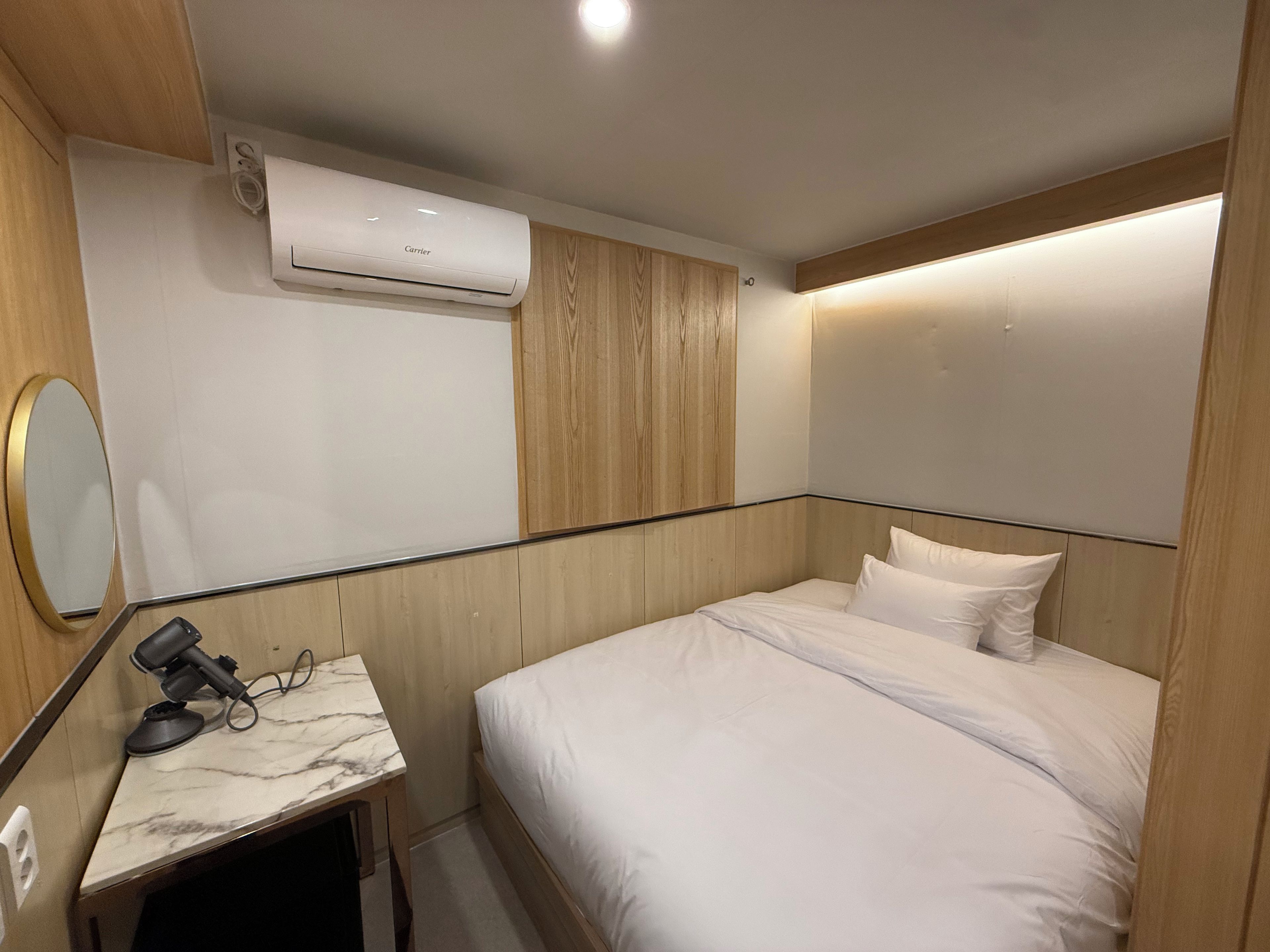 Ein Hotelzimmer mit einem Bett, einem kleinen Schreibtisch mit Föhn, einer Klimaanlage und einem Spiegel.