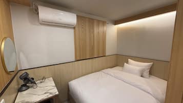 Ein Hotelzimmer mit einem Bett, einem kleinen Schreibtisch mit Föhn, einer Klimaanlage und einem Spiegel.
