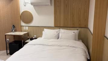 Habitación de hotel con una cama grande, una mesita de noche, aire acondicionado montado en la pared y un espejo circular.