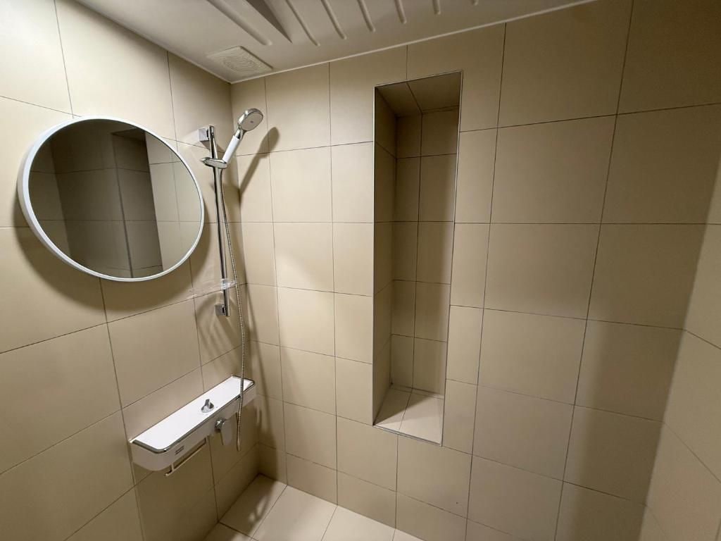 Un baño con ducha, espejo y una pequeña estantería.