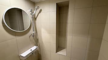 Un baño con ducha, espejo y una pequeña estantería.