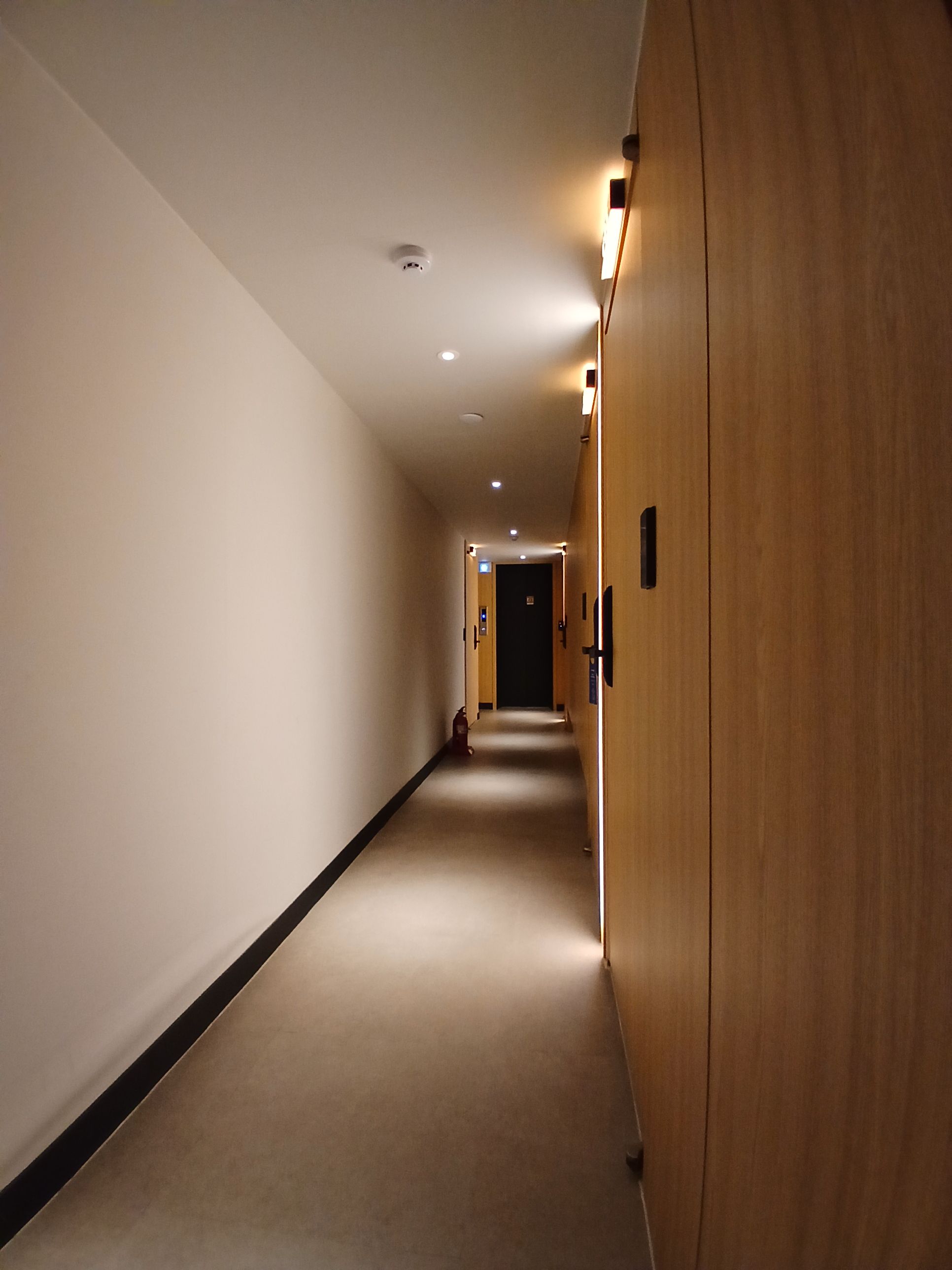 Ein langer, schmaler Hotelgang mit Holztüren auf der einen Seite und einer schlichten Wand auf der anderen.