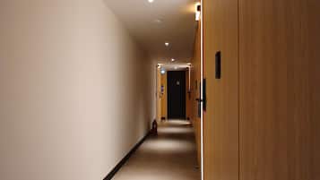 Ein langer, schmaler Hotelgang mit Holztüren auf der einen Seite und einer schlichten Wand auf der anderen.