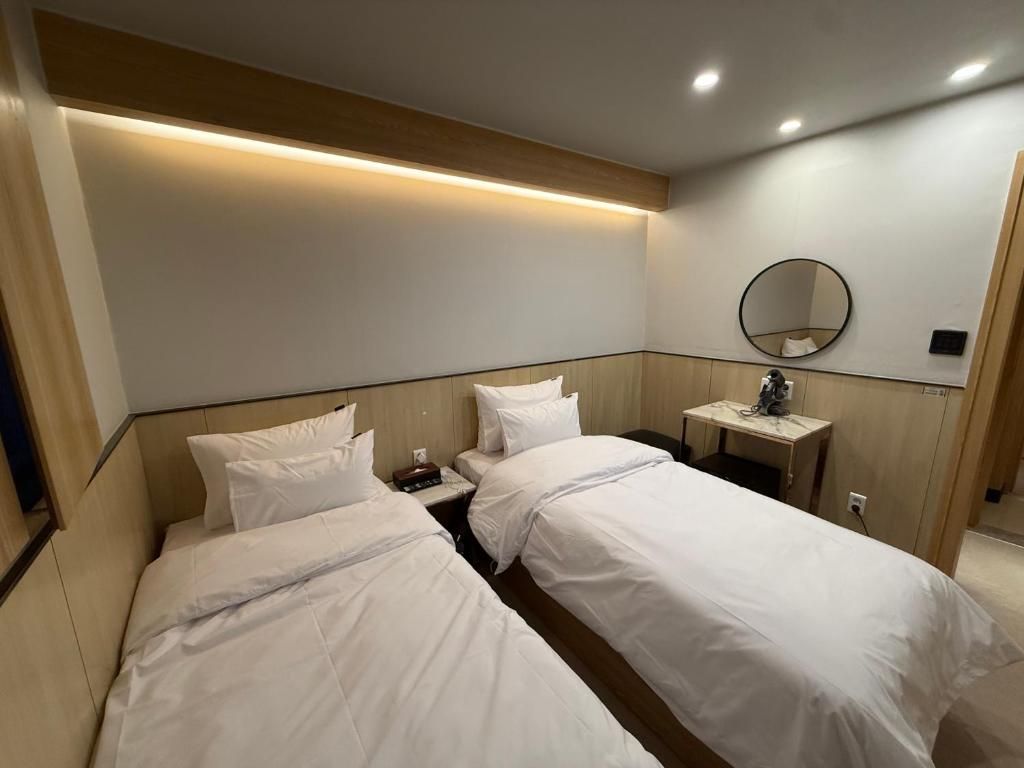 Habitación de hotel con dos camas, una mesita de noche, un espejo y una lámpara de pared.