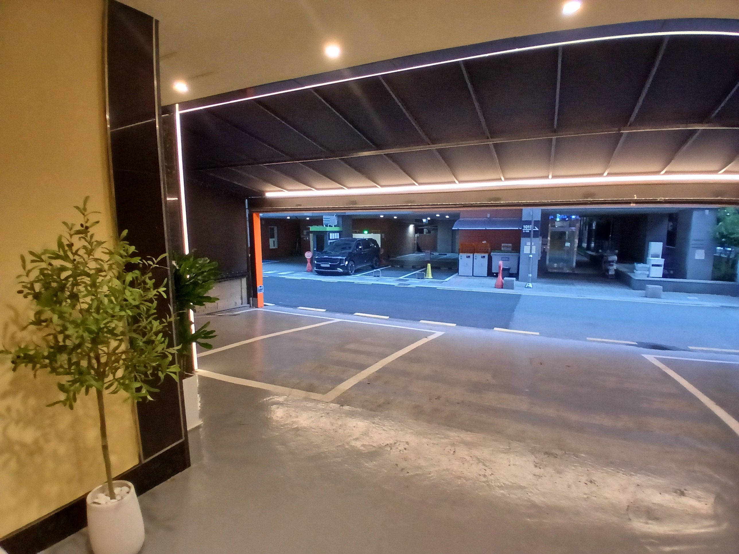 Einfahrt einer Parkgarage mit einem Blumentopf, einem Auto und einem Gebäude im Hintergrund, auf dem das Schild '1011' zu sehen ist.