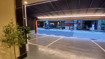 Einfahrt einer Parkgarage mit einem Blumentopf, einem Auto und einem Gebäude im Hintergrund, auf dem das Schild '1011' zu sehen ist.