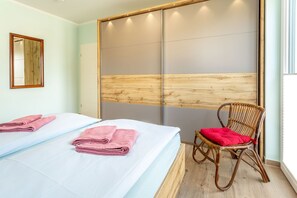 Een hotelkamer met twee bedden, een houten hoofdbord, een rieten stoel met een rode kussens en een raam met zonwering.